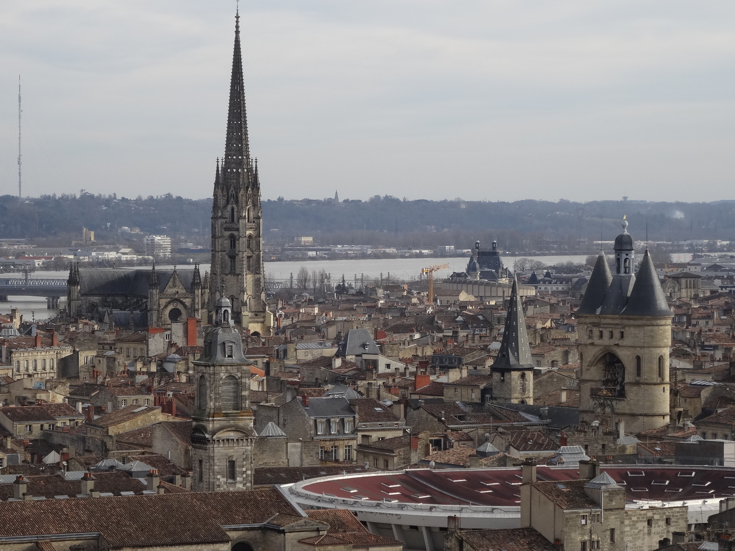 Vue d’une partie du secteur sauvegardé de Bordeaux depuis les toits. Garonne et flèche Saint-Michel en arrière plan. Toit du Palais des Sports au premier plan. Grosse cloche, monuments historiques et immeubles d’habitation. 